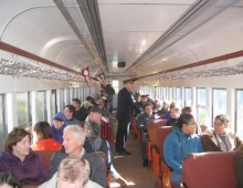 A group of older people are on a train with conductor/professor Frank Moscatelli as a guide.